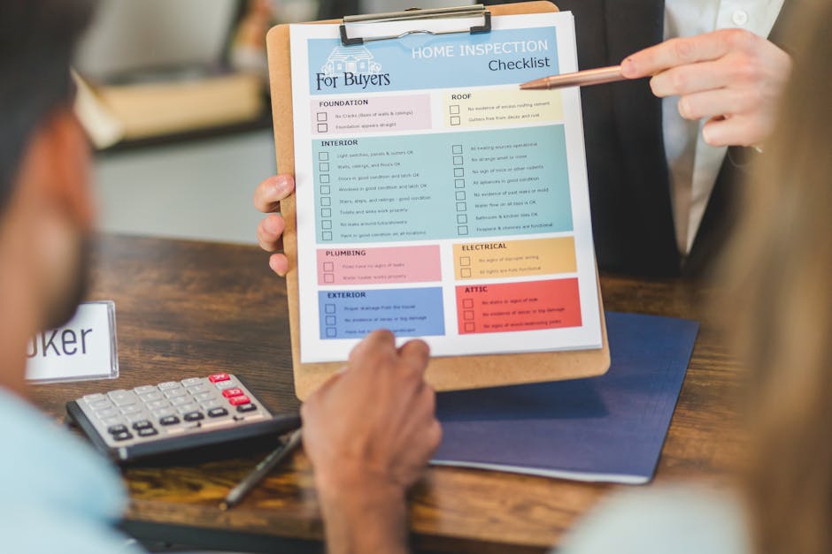 In the foreground, a person is seated at a wooden table while another individual, standing to the right, is pointing at a home inspection checklist attached to a clipboard. The checklist features various sections such as foundation, interior, plumbing, exterior, roof, electrical, and attic, each with multiple checkboxes and colored headers including blue, pink, yellow, and red. The seated individual has a hand resting near a calculator with visible red and black buttons, and a black pen lies on the table close to their hand. The background is slightly blurred, suggesting an indoor setting, possibly an office or consultation space. The scene conveys an environment focused on property inspections or estate clearance, consistent with the services provided by House Clearance Pimlico, relevant to private waste handling or on-site clearance activities, with the focus on detailed assessment before rubbish removal or disposal planning in Pimlico or Churchill Gardens areas.